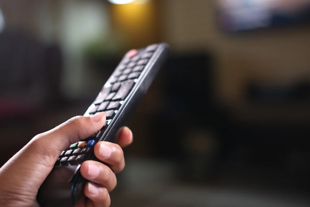 TV remote control held up in front of a television, used for on-screen text entry