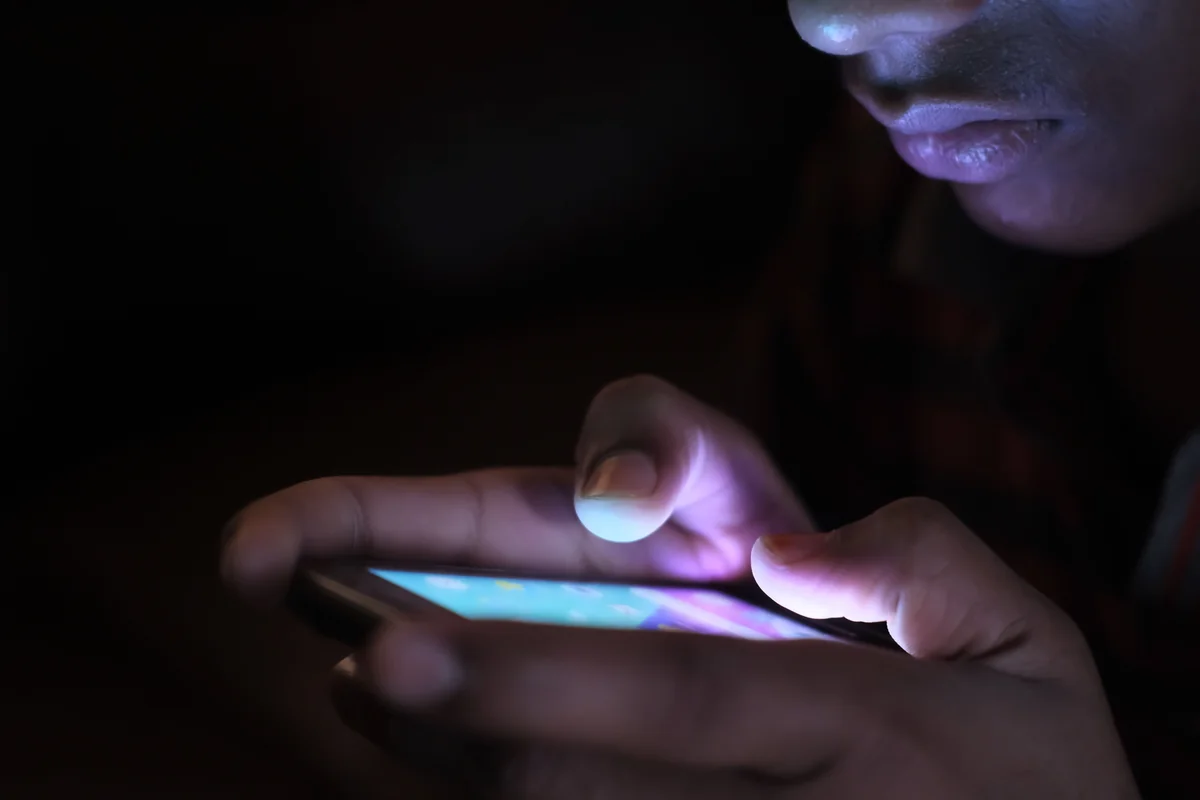 Close-up van handen met een smartphone met een oplichtend scherm binnenshuis