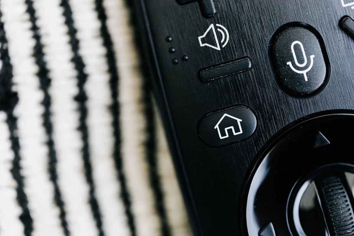 Close-up of a smart TV remote control with home, microphone and volume buttons