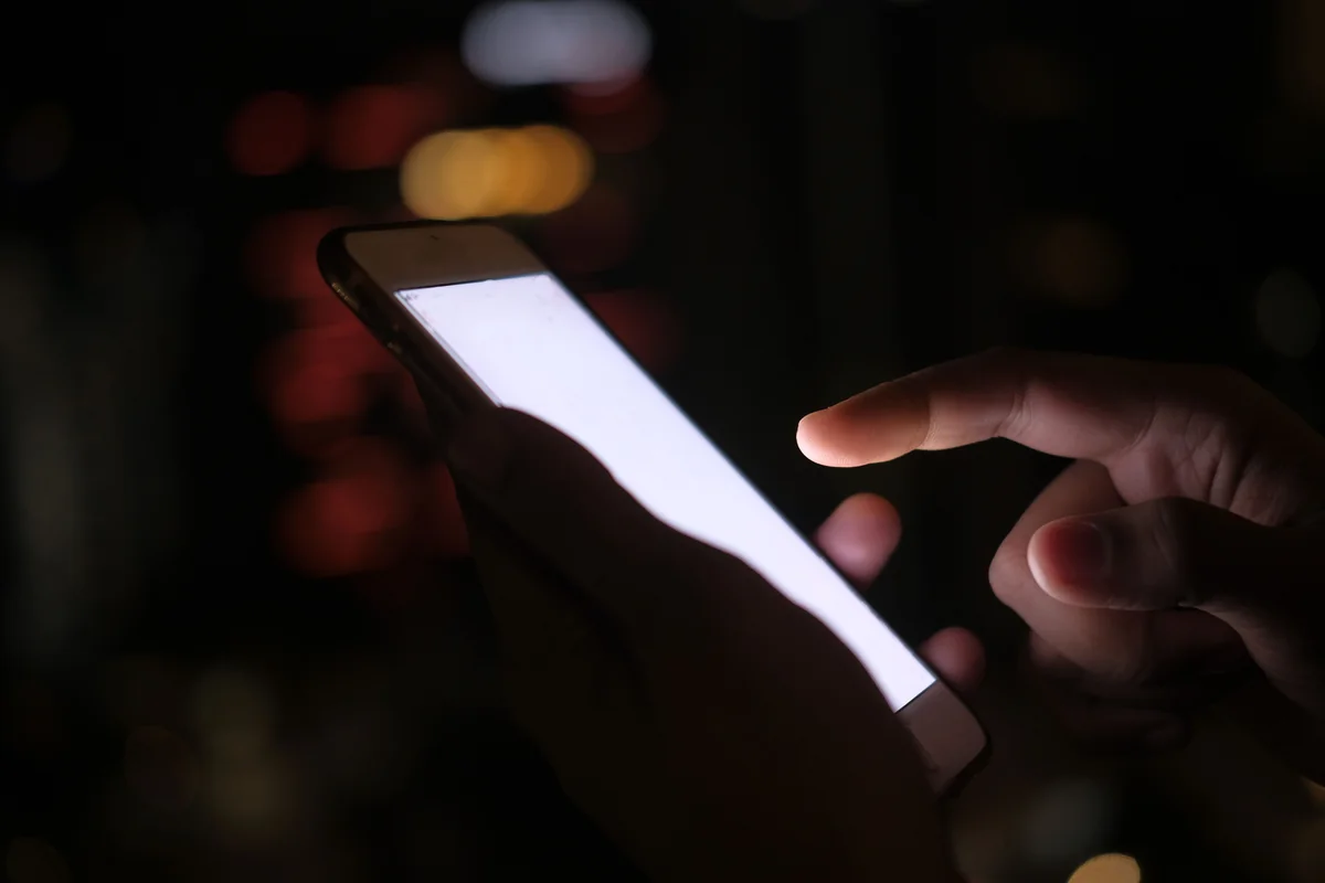 Hand hält ein iPhone mit leuchtendem Display in einem dunklen Raum