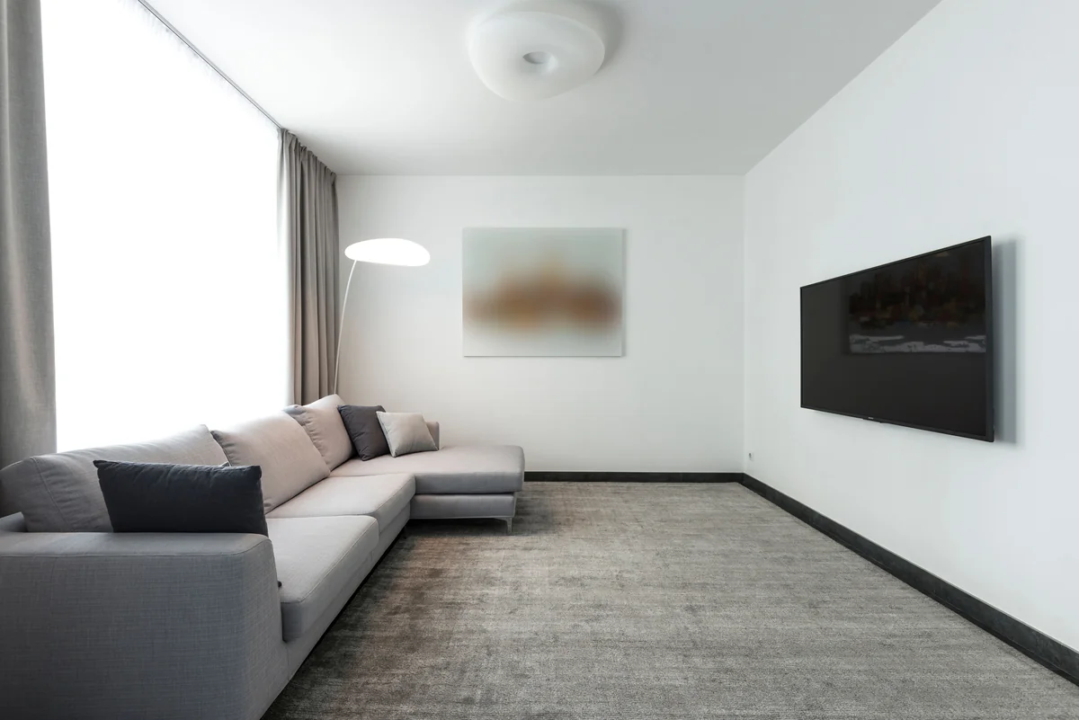 Nowoczesny minimalistyczny salon z telewizorem zamontowanym na ścianie i szarą sofą