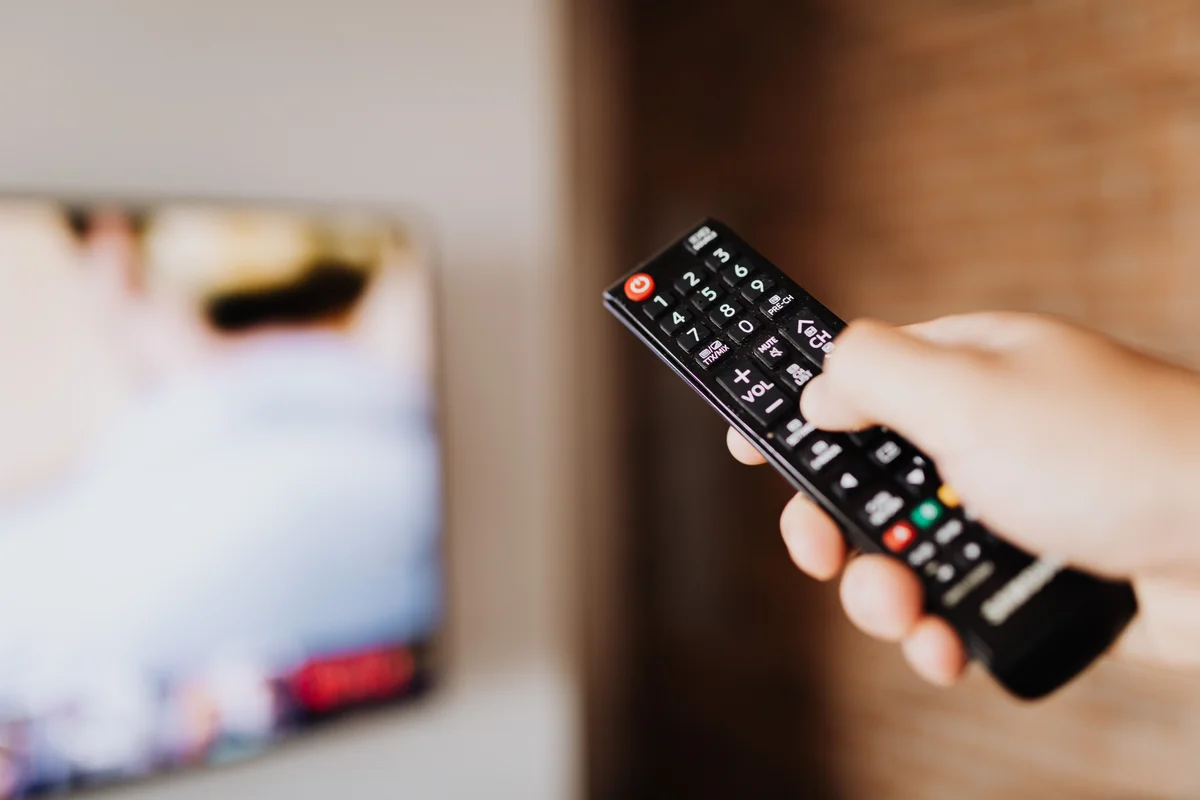 Person richtet eine Fernbedienung auf einen Fernsehbildschirm, um durch eine App zu navigieren