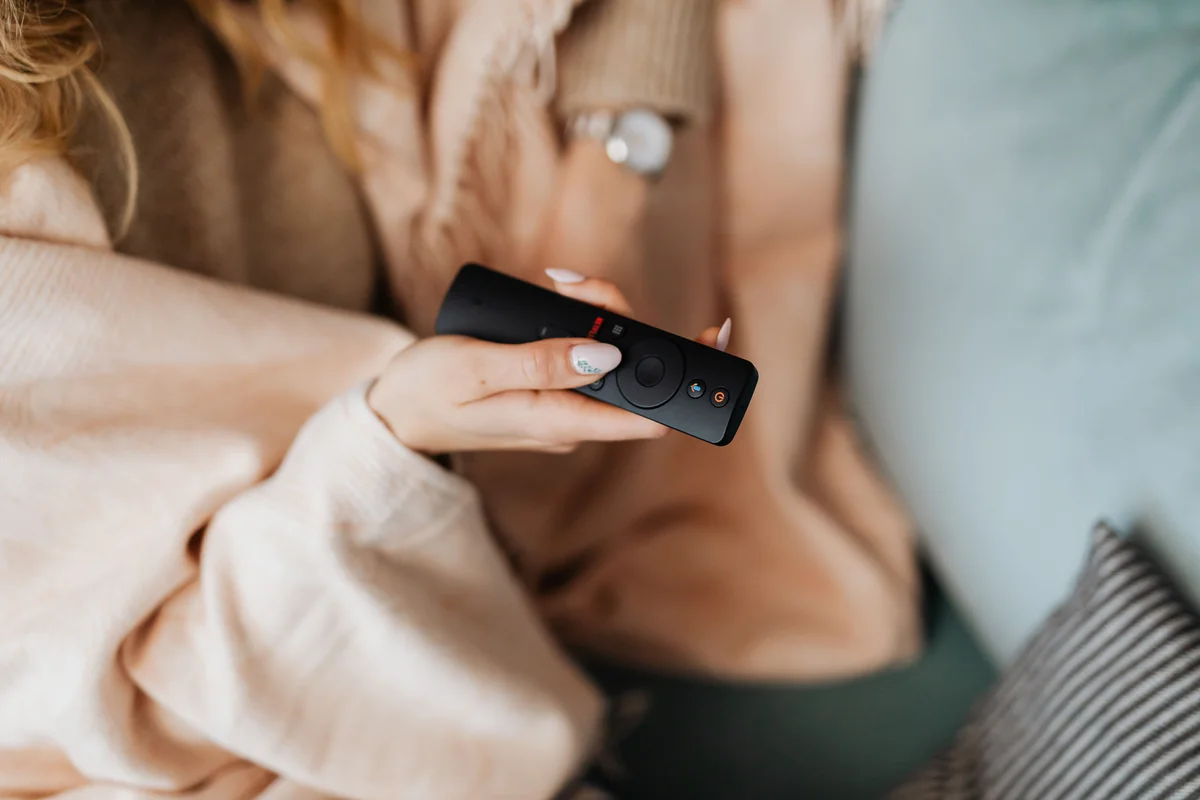 Hand hält eine moderne Fernbedienung vor einem Fernseher