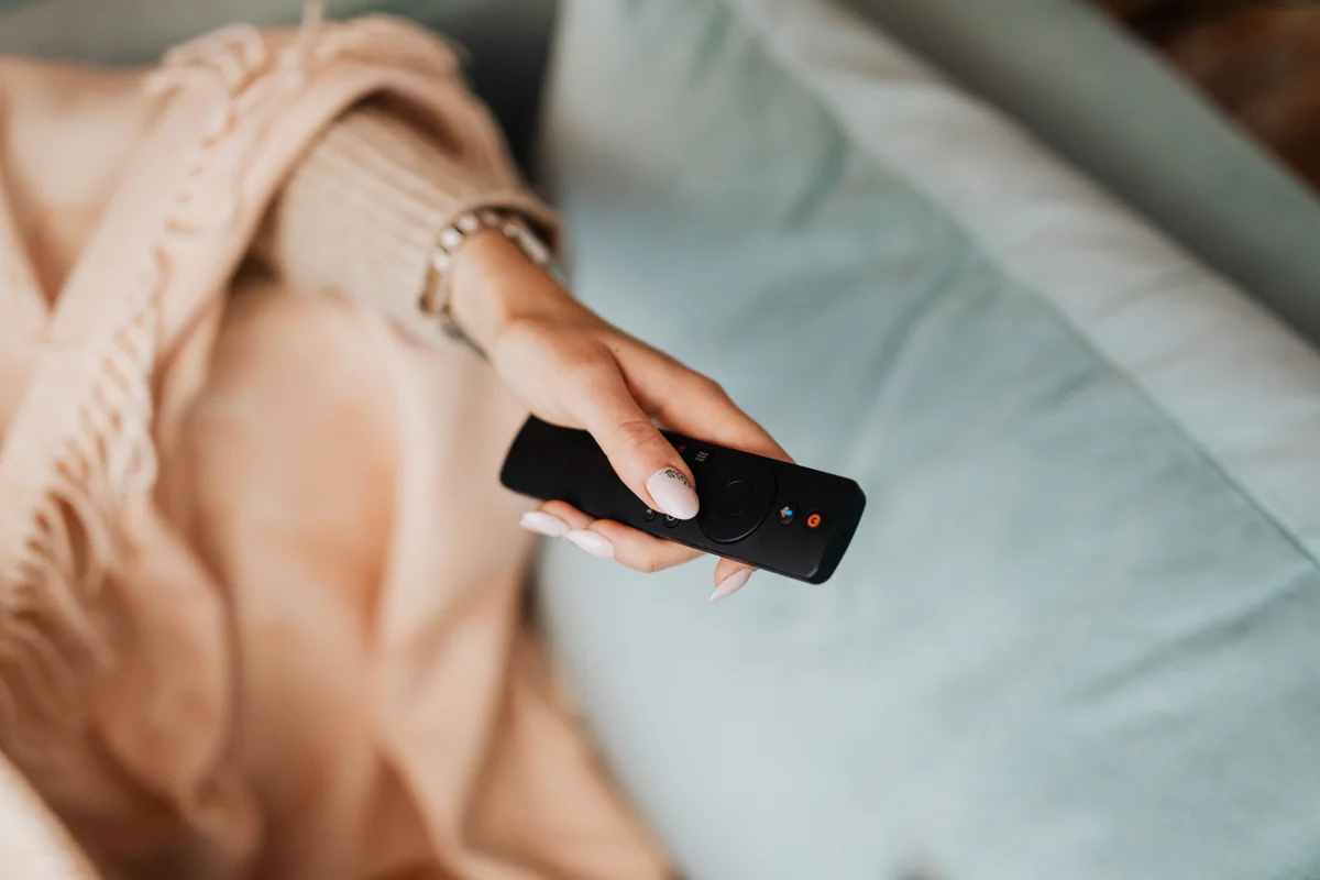 Nahaufnahme einer Hand, die eine Streaming-Fernbedienung mit Richtungstasten hält