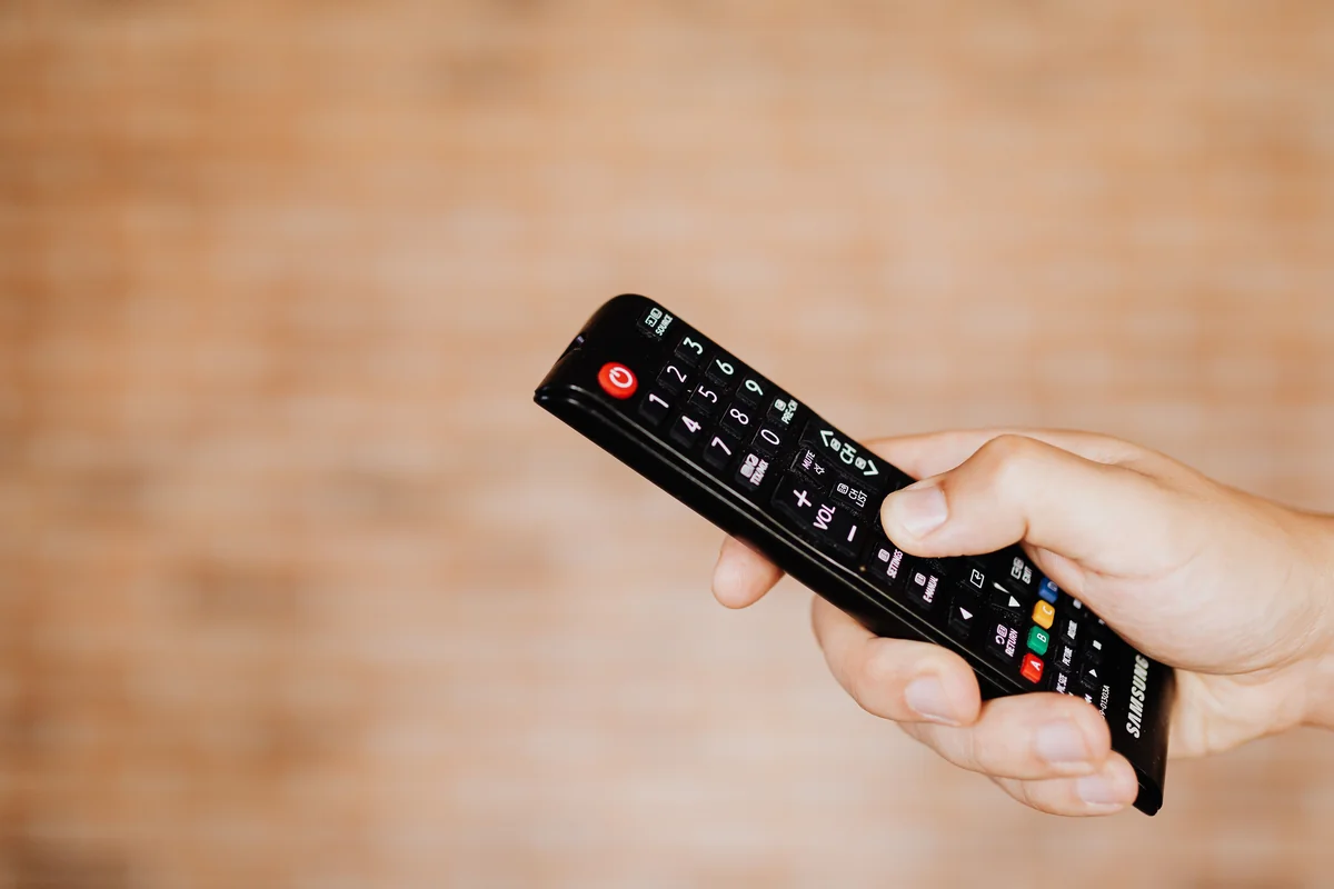 Nahaufnahme einer Hand, die eine Fernbedienung auf einen Fernseher richtet