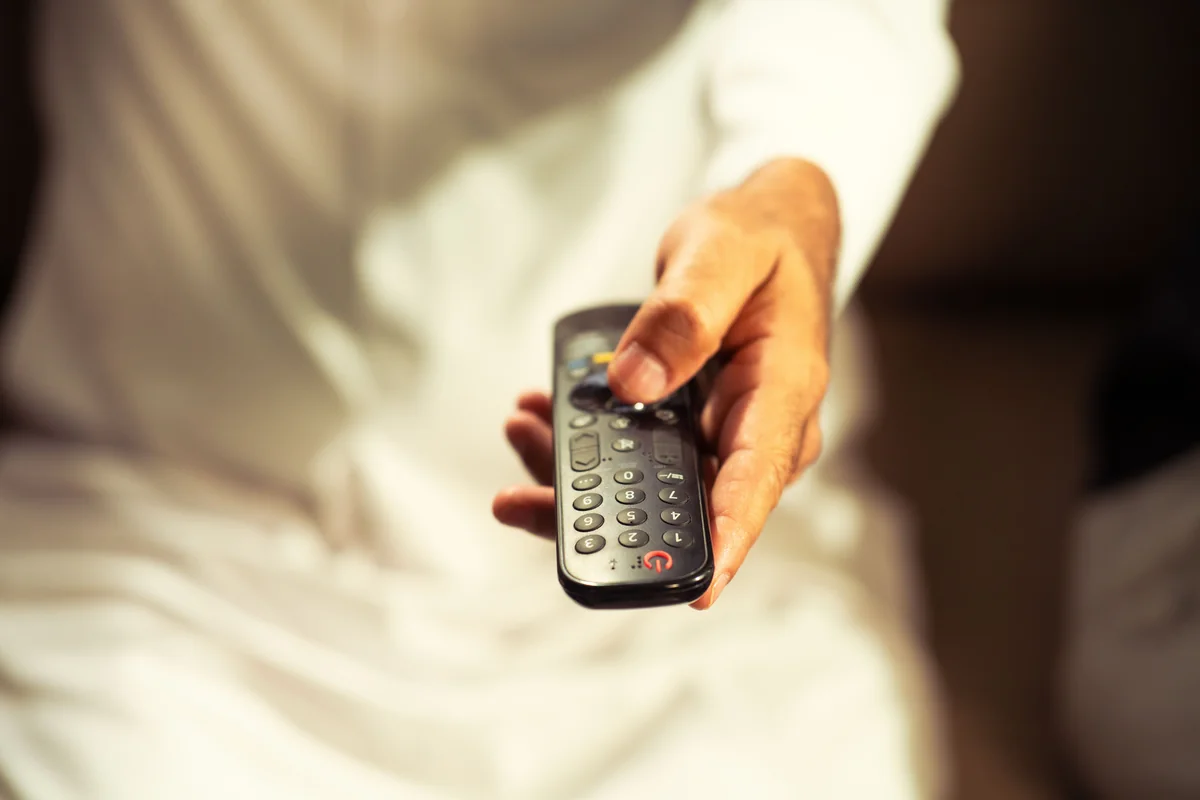 Person nutzt eine TV-Fernbedienung, um Text auf einem Fernsehbildschirm einzugeben